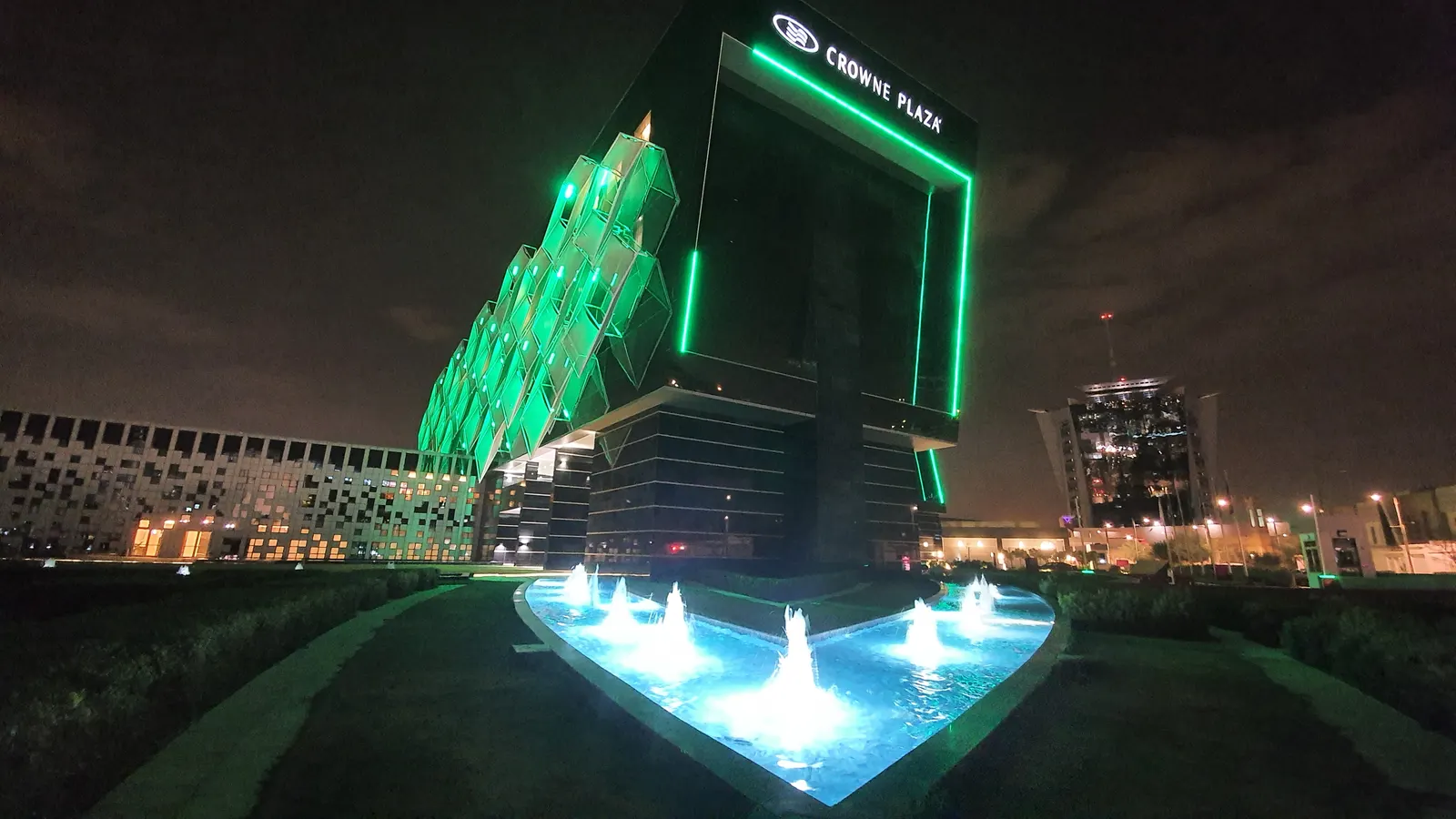 Crowne Plaza Riyadh at night, with illuminated fountains in front of the green-lit facade